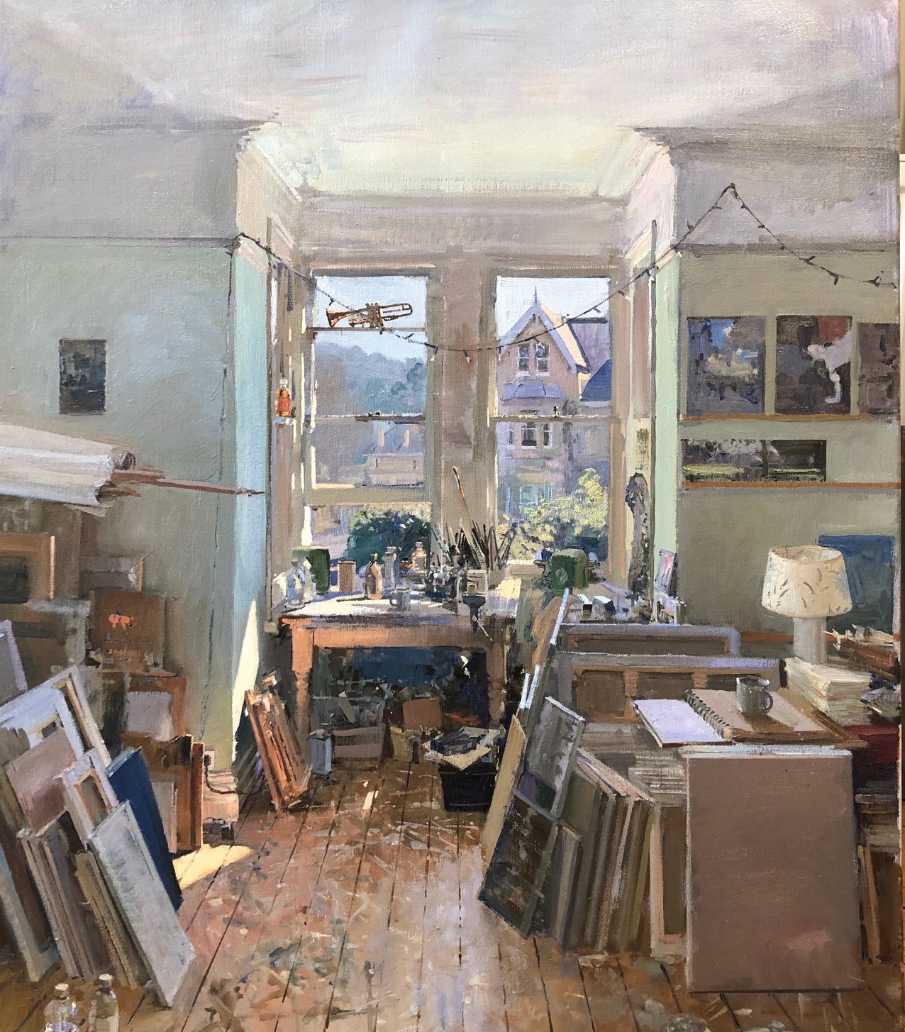 A painting of a painter’s studio, the wooden floor covered with leaning canvases and light streaming in a window