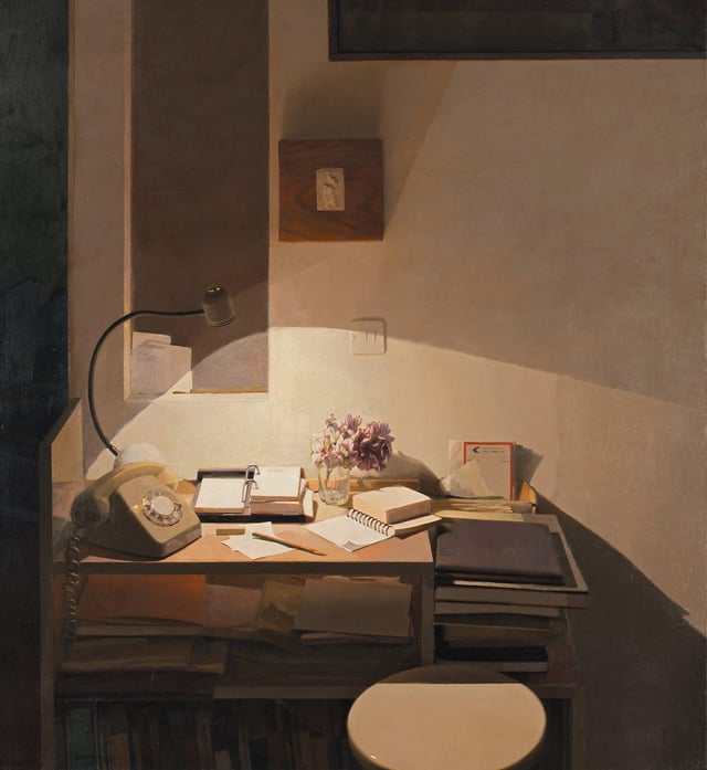 Still life of a cluttered but orderly desk with rotary phone to the side lit by a desk lamp