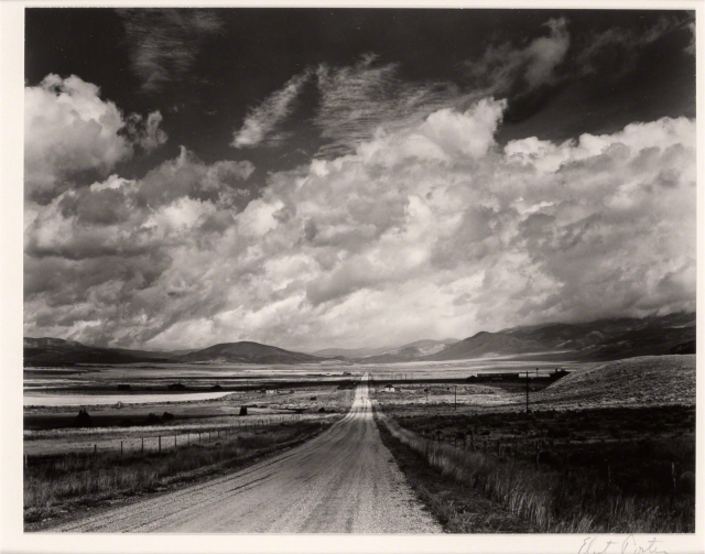 black and white desert landscape photo with big sky and dirt road cutting through 