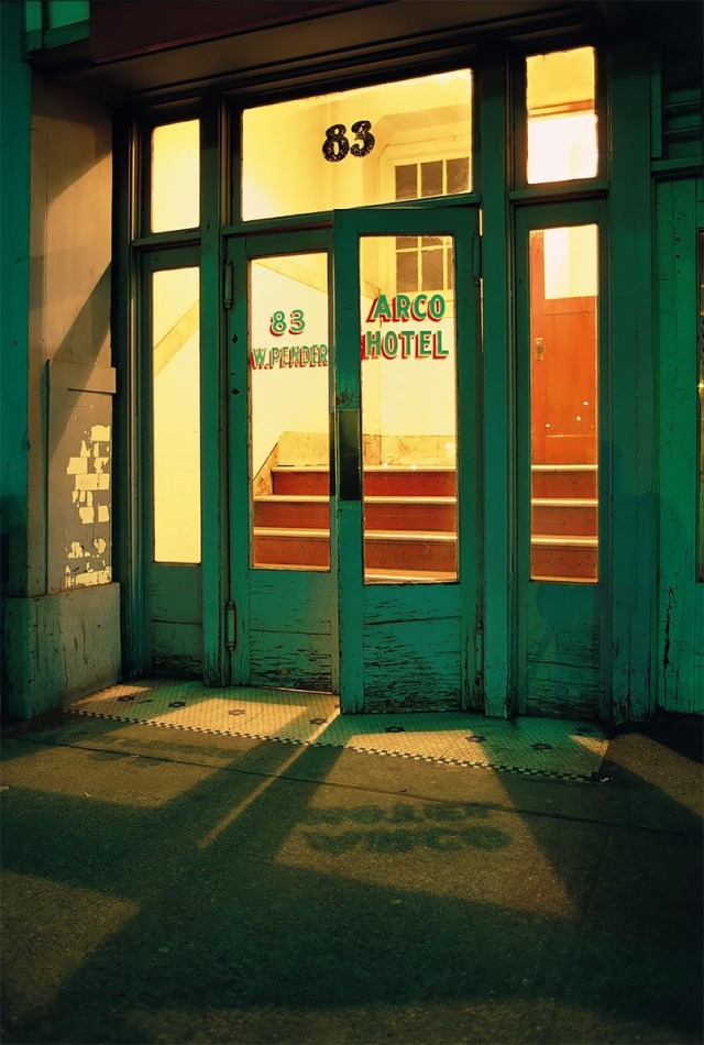 A photo of a a set of double doors with one door slightly ajar. The glass has 'Arco Hotel' written on it and yellow light is streaming out from inside.