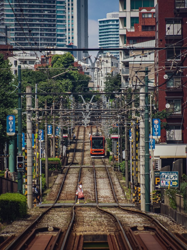 Lovely densely urban scene of train tracks, maybe Tokyo, with a figure walking across and a train in the background. 