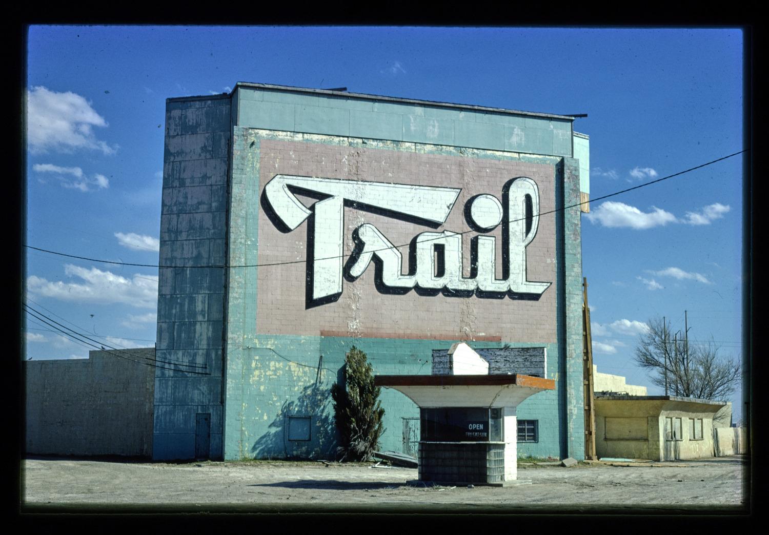 A color photograph of a building featuring the word "Trail" in large, stylized white lettering, with a small, mid-century ticket booth in the foreground.