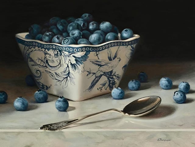 Still life painting of a decorative blue and white ceramic bowl overflowing with fresh blueberries. A silver spoon and scattered loose blueberries sit on a marble surface in front of the bowl against a dark background.